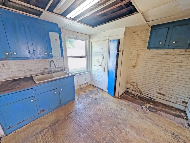 kitchen featuring blue cabinetry, a sink, and brick wall