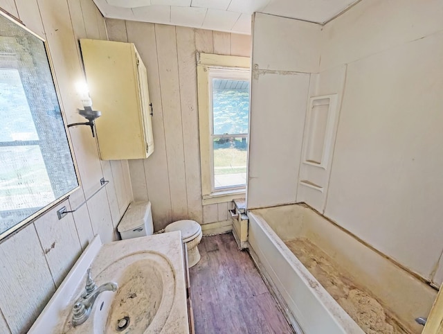 full bathroom with wood finished floors, toilet, wood walls, and a sink