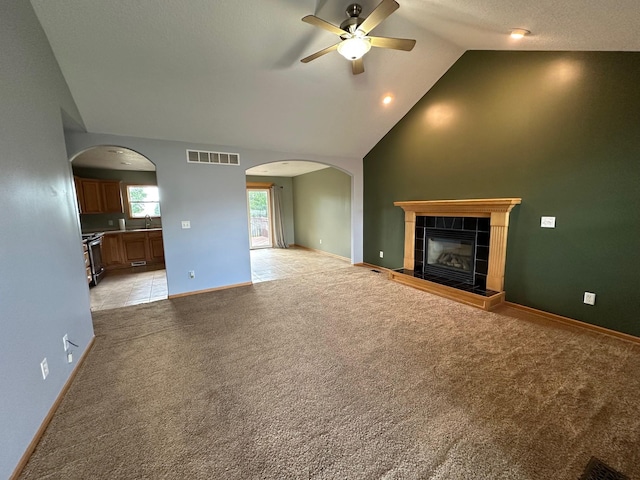 322 N 15th Ave, Winterset, IA 50273 - unfurnished living room with a ceiling fan, a tiled fireplace, arched walkways, vaulted ceiling, and a sink