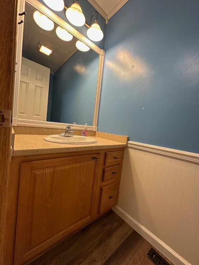 322 N 15th Ave, Winterset, IA 50273 - bathroom featuring wood finished floors, a wainscoted wall, vanity, crown molding, and lofted ceiling
