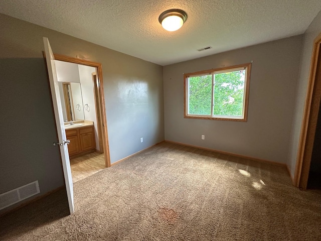 322 N 15th Ave, Winterset, IA 50273 - unfurnished bedroom with light colored carpet, a sink, a textured ceiling, baseboards, and ensuite bath