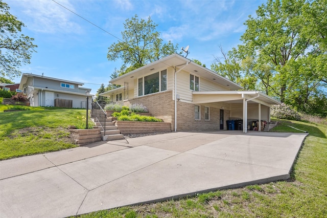 rear view of property featuring brick siding, driveway, a lawn, and a carport