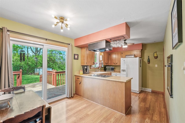 kitchen featuring white fridge with ice dispenser, stainless steel microwave, ventilation hood, a peninsula, and light countertops