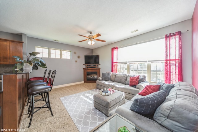 living room with carpet, a ceiling fan, a glass covered fireplace, baseboards, and a textured ceiling