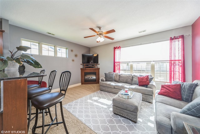 living room featuring carpet flooring, a ceiling fan, baseboards, and a glass covered fireplace
