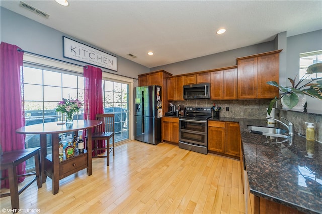 kitchen with stainless steel appliances, a sink, decorative backsplash, brown cabinetry, and light wood-style floors