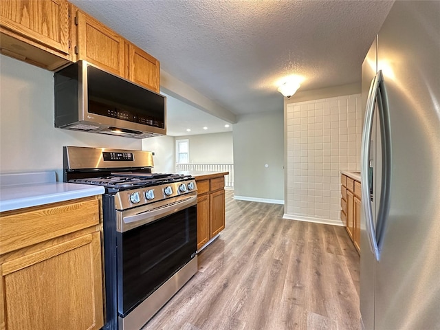 3429 54th St, Des Moines, IA 50310 - kitchen featuring stainless steel appliances, light wood-style floors, light countertops, a textured ceiling, and brown cabinetry