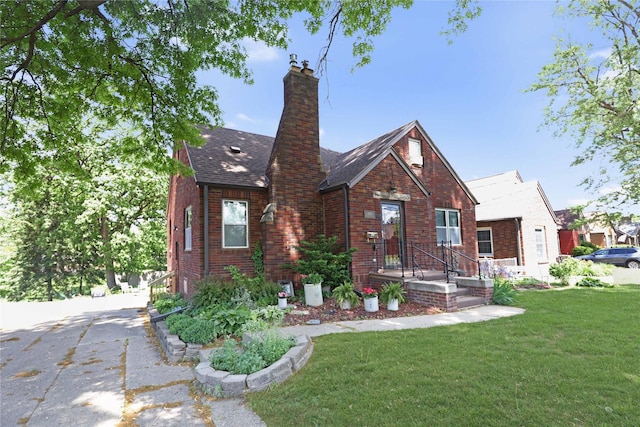 tudor house with a front yard, brick siding, a chimney, and a shingled roof