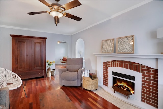 living room featuring wood finished floors, a brick fireplace, ceiling fan, and ornamental molding