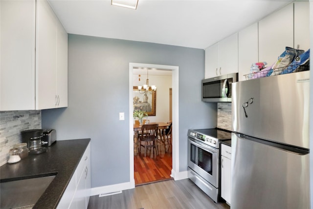kitchen featuring appliances with stainless steel finishes, light wood-style floors, dark countertops, and a chandelier