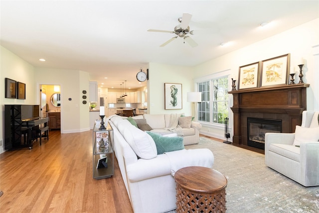 living area with light wood-style floors, baseboards, a ceiling fan, recessed lighting, and a fireplace with flush hearth