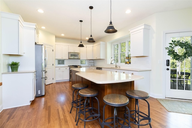 kitchen with appliances with stainless steel finishes, a kitchen island, a sink, a kitchen breakfast bar, and wood finished floors