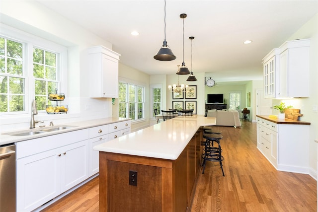kitchen featuring a sink, dishwasher, light wood finished floors, a kitchen bar, and white cabinetry