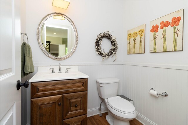 bathroom featuring a wainscoted wall, toilet, vanity, and wood finished floors