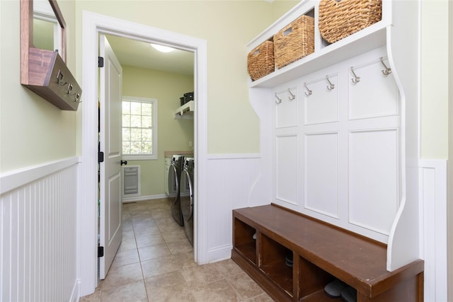 mudroom featuring separate washer and dryer, a wainscoted wall, light tile patterned floors, and a decorative wall