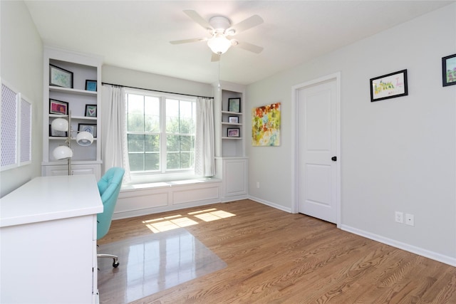unfurnished office featuring wood finished floors, a ceiling fan, built in shelves, and baseboards