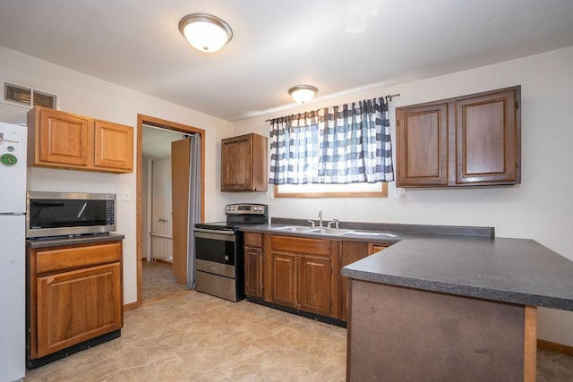 1209 Spencer St, Grinnell, IA 50112 - kitchen with stainless steel appliances, dark countertops, a sink, a peninsula, and brown cabinetry