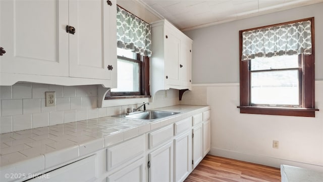 kitchen featuring a sink, tile countertops, white cabinets, and light wood-style floors