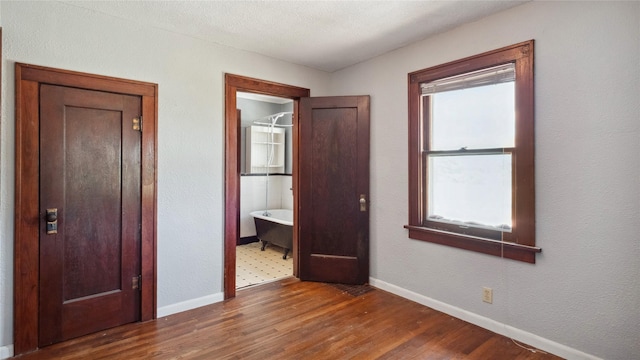 unfurnished bedroom featuring wood finished floors, baseboards, and ensuite bath