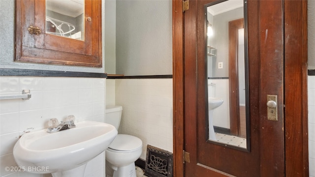 bathroom featuring tile walls, a sink, toilet, ornamental molding, and wainscoting