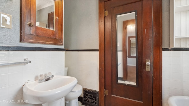 half bathroom with tile walls, toilet, a sink, a wainscoted wall, and a textured wall