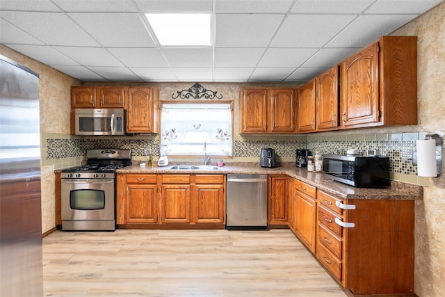 630 E Clay St, Osceola, IA 50213 - kitchen with appliances with stainless steel finishes, a sink, brown cabinetry, light wood-style flooring, and a paneled ceiling