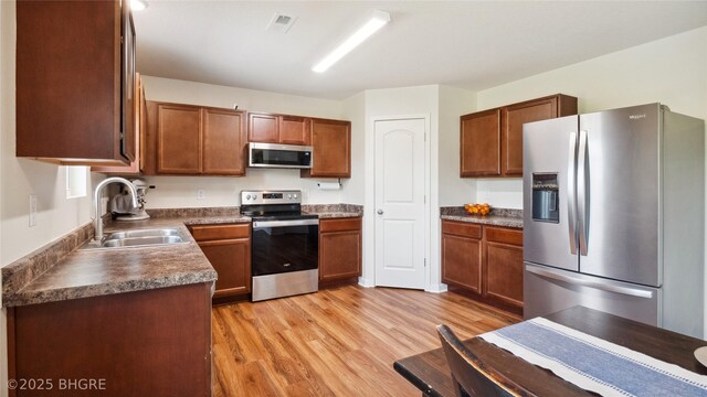 1508 E Euclid Ave, Indianola, IA 50125 - kitchen featuring stainless steel appliances, a sink, light wood-style flooring, dark countertops, and brown cabinetry