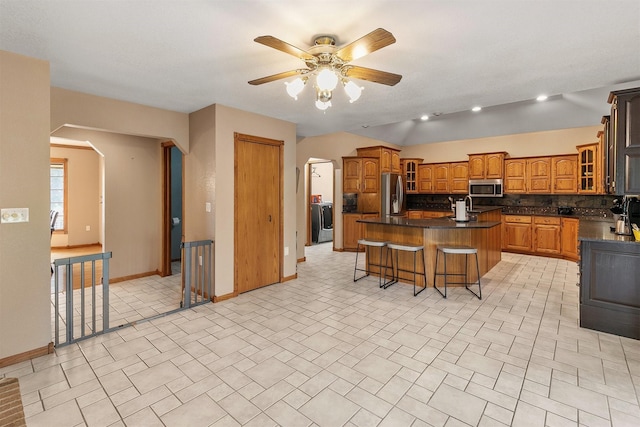 913 W 18th St S, Newton, IA 50208 - kitchen featuring stainless steel appliances, dark countertops, a kitchen island with sink, baseboards, and brown cabinetry
