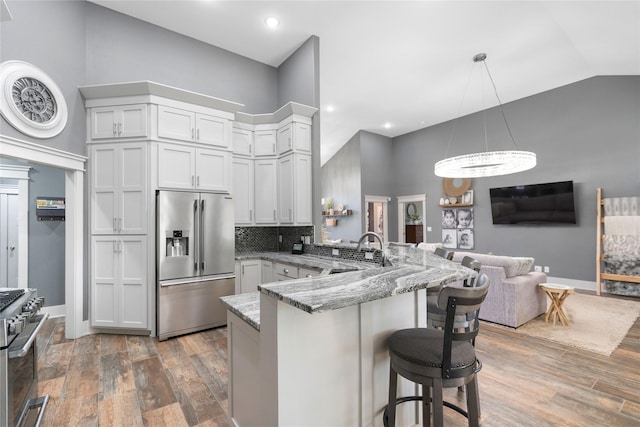 kitchen with appliances with stainless steel finishes, a peninsula, a sink, a chandelier, and light stone counters