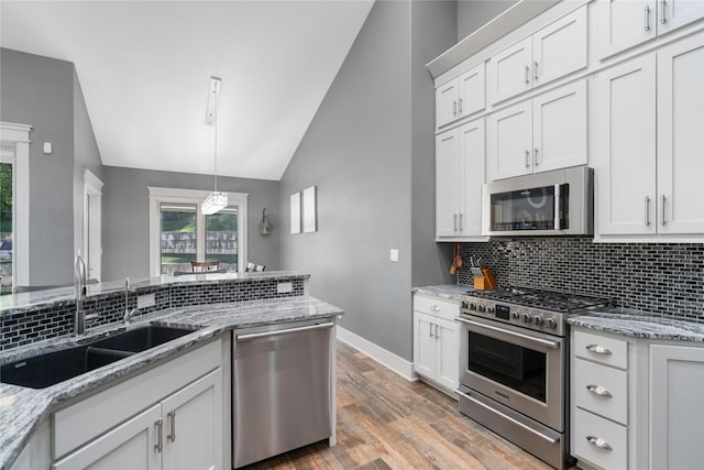 kitchen with appliances with stainless steel finishes, lofted ceiling, a sink, baseboards, and backsplash