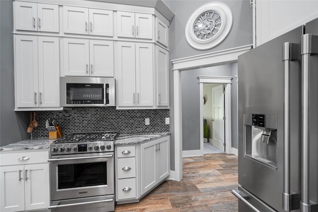 kitchen with appliances with stainless steel finishes, light wood finished floors, backsplash, and light stone counters