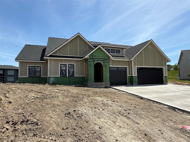property in mid-construction featuring an attached garage, driveway, board and batten siding, and a shingled roof
