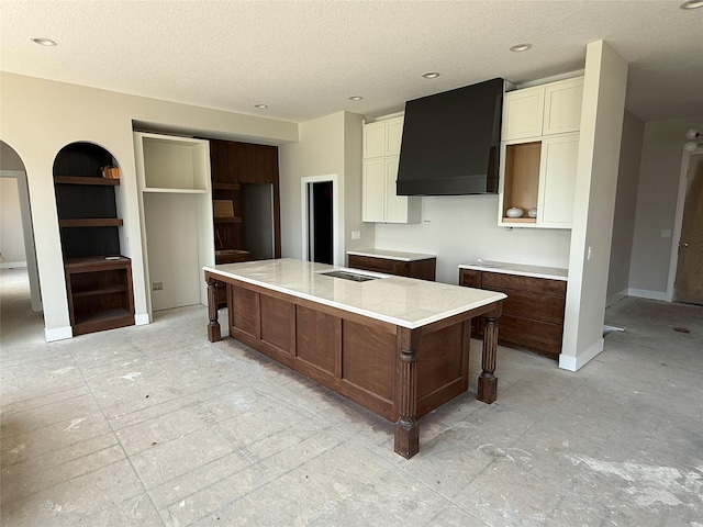 kitchen featuring wall chimney exhaust hood, a large island, a textured ceiling, white cabinets, and light countertops