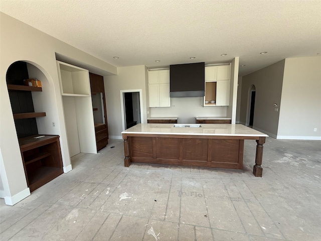 kitchen with a textured ceiling, baseboards, premium range hood, white cabinets, and arched walkways