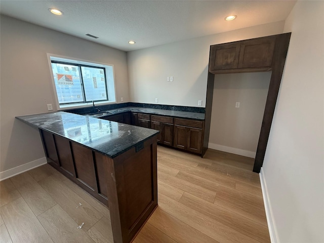 1128 NW 29th Ct, Grimes, IA 50111 - kitchen featuring a peninsula, dark stone counters, light wood-type flooring, dark brown cabinets, and recessed lighting