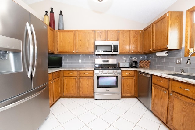 kitchen with stainless steel appliances, a sink, lofted ceiling, tasteful backsplash, and brown cabinets