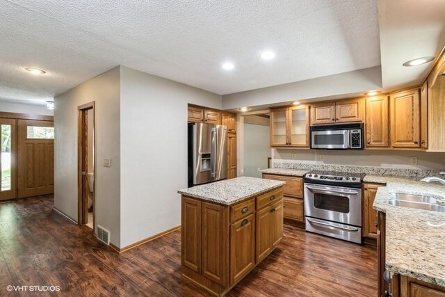 6406 Theresa Dr, Johnston, IA 50131 - kitchen featuring appliances with stainless steel finishes, a sink, dark wood-type flooring, a textured ceiling, and a kitchen island
