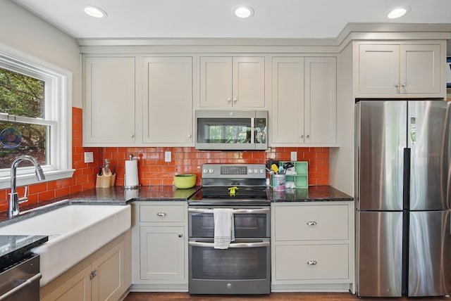 1919 Arlington Ave, Des Moines, IA 50314 - kitchen featuring stainless steel appliances, a sink, decorative backsplash, dark stone counters, and white cabinets