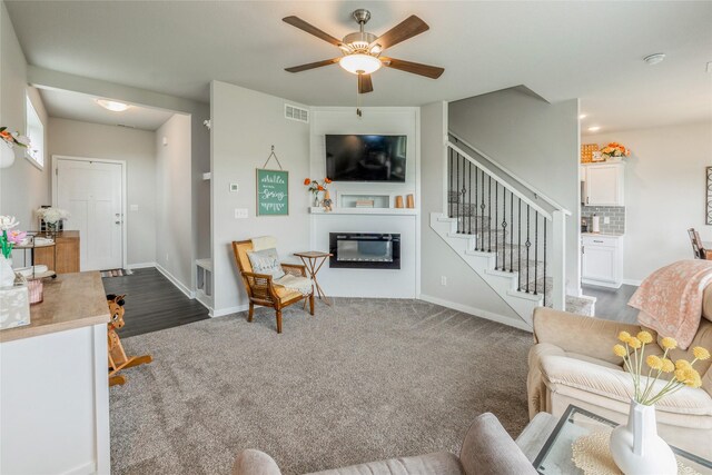 217 NE Glendale Ln, Ankeny, IA 50021 - living room with a glass covered fireplace, stairway, ceiling fan, dark carpet, and baseboards