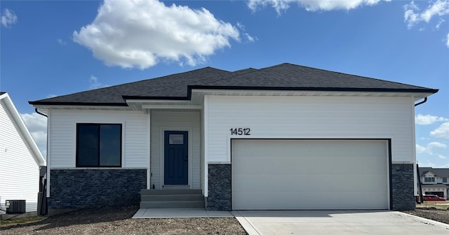 14512 Northpark Dr, Urbandale, IA 50111 - view of front of home with stone siding, concrete driveway, central air condition unit, roof with shingles, and an attached garage