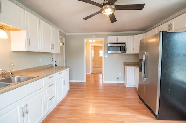 101 E Cronkhite St, Knoxville, IA 50138 - kitchen featuring stainless steel appliances, ceiling fan, white cabinetry, light wood-style floors, and ornamental molding