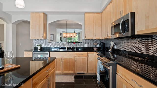 201 Grand Ave Unit 109, Des Moines, IA 50309 - kitchen with appliances with stainless steel finishes, a sink, light brown cabinetry, dark countertops, and decorative backsplash