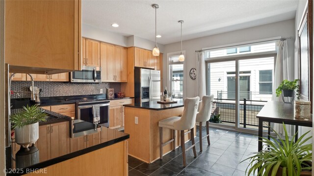 201 Grand Ave Unit 109, Des Moines, IA 50309 - kitchen featuring stainless steel appliances, dark countertops, decorative backsplash, light brown cabinets, and a center island