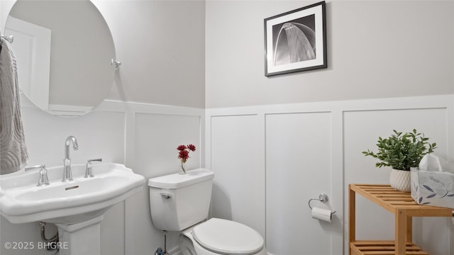 201 Grand Ave Unit 109, Des Moines, IA 50309 - half bathroom featuring a decorative wall, a wainscoted wall, toilet, and a sink