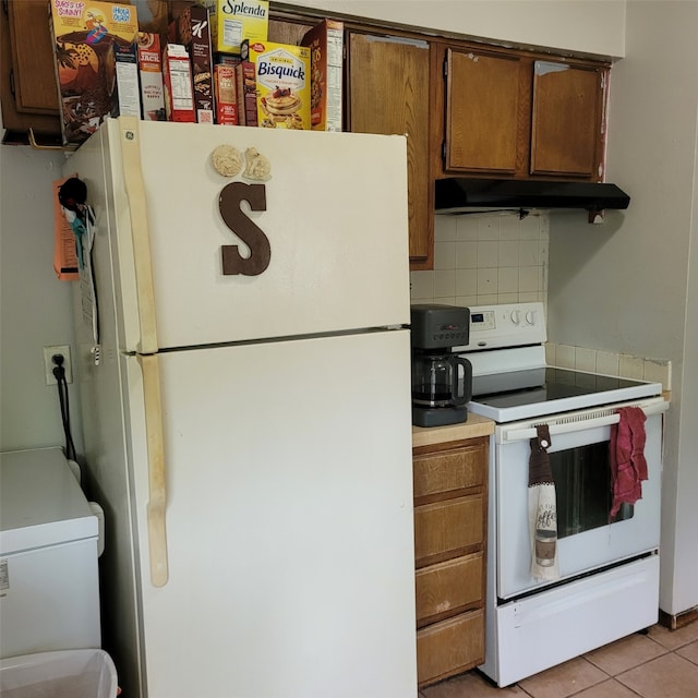 1850 King Ave, Des Moines, IA 50320 - kitchen with white appliances, under cabinet range hood, backsplash, brown cabinetry, and light tile patterned floors