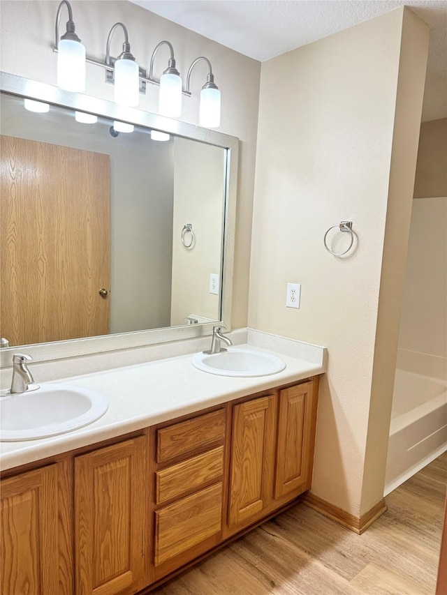 10141 Sutton Dr Unit 7, Urbandale, IA 50322 - bathroom featuring wood finished floors, double vanity, a tub, and baseboards