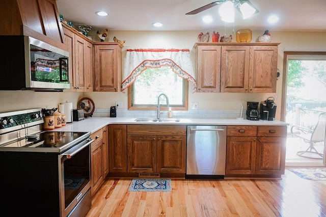 kitchen featuring stainless steel appliances, a sink, light countertops, a ceiling fan, and light wood finished floors