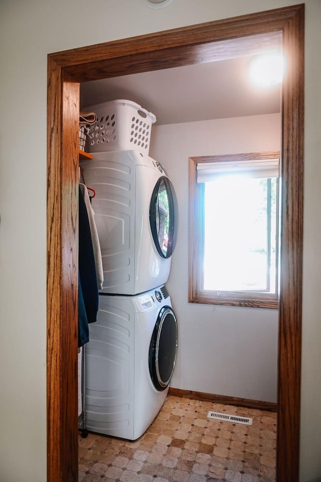 clothes washing area with estacked washer and dryer, light floors, and baseboards