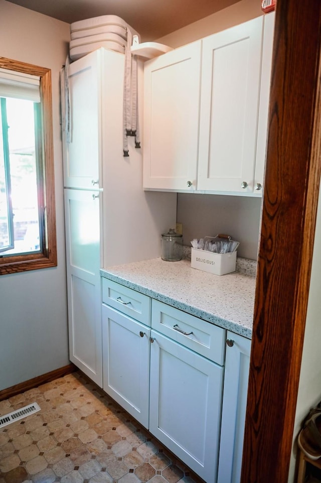kitchen with white cabinets, light stone counters, light floors, and baseboards