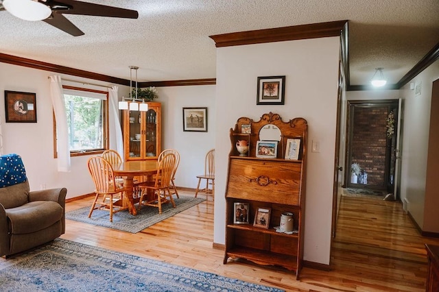 dining area featuring ornamental molding, a textured ceiling, a ceiling fan, light wood-style flooring, and baseboards
